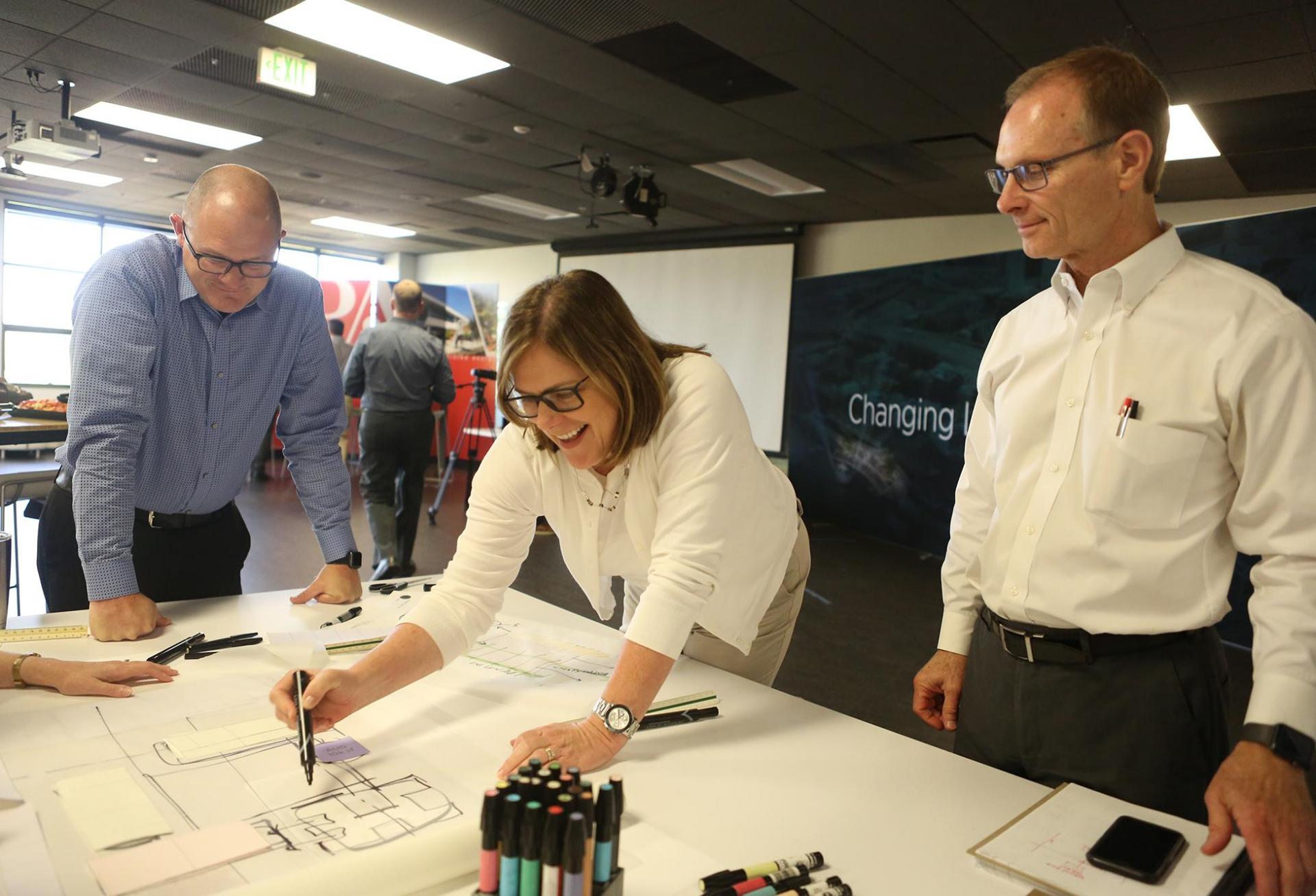 LPA Design Studios CEO Wendy Rogers leaning over a table working on a blueprint with a man on either side of her. 