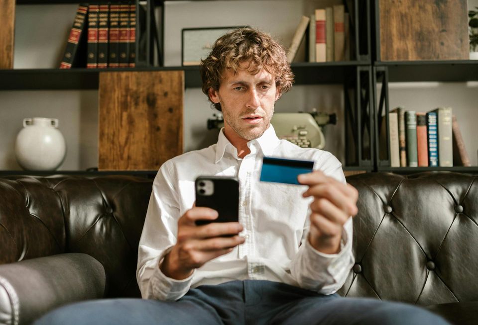 Man holding credit card and phone, looking overwhelmed
