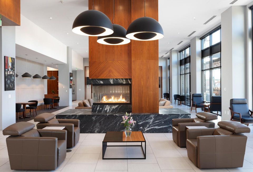 A high-resolution photo of the interior of 24Fifty at University Park, with four armchairs, a fireplace and three overhead lights in a modern setting.