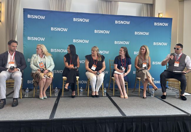 From left to right, speakers on a stage: Madison Rose's Adam Pines, Becknell Industrial's Paige Steers, Cushman & Wakefield's Sheila Acar, 1905 New Media's Kaysha Hanock, Stream Realty Partners' Marissa Rupert, Taylor Johnson Public Relations' Emily Johnson and Bisnow's Zak Guysenir.