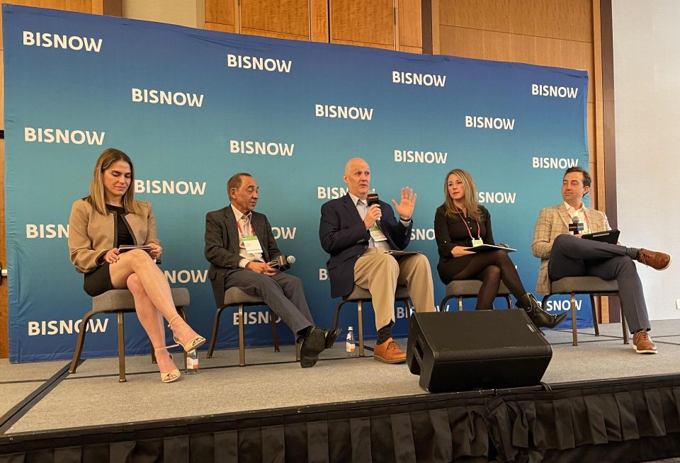 A photograph of a panel discussion at Bisnow's Denver-Boulder Life Sciences Summit. Speakers sit in front of a Bisnow-branded step-and-repeat.