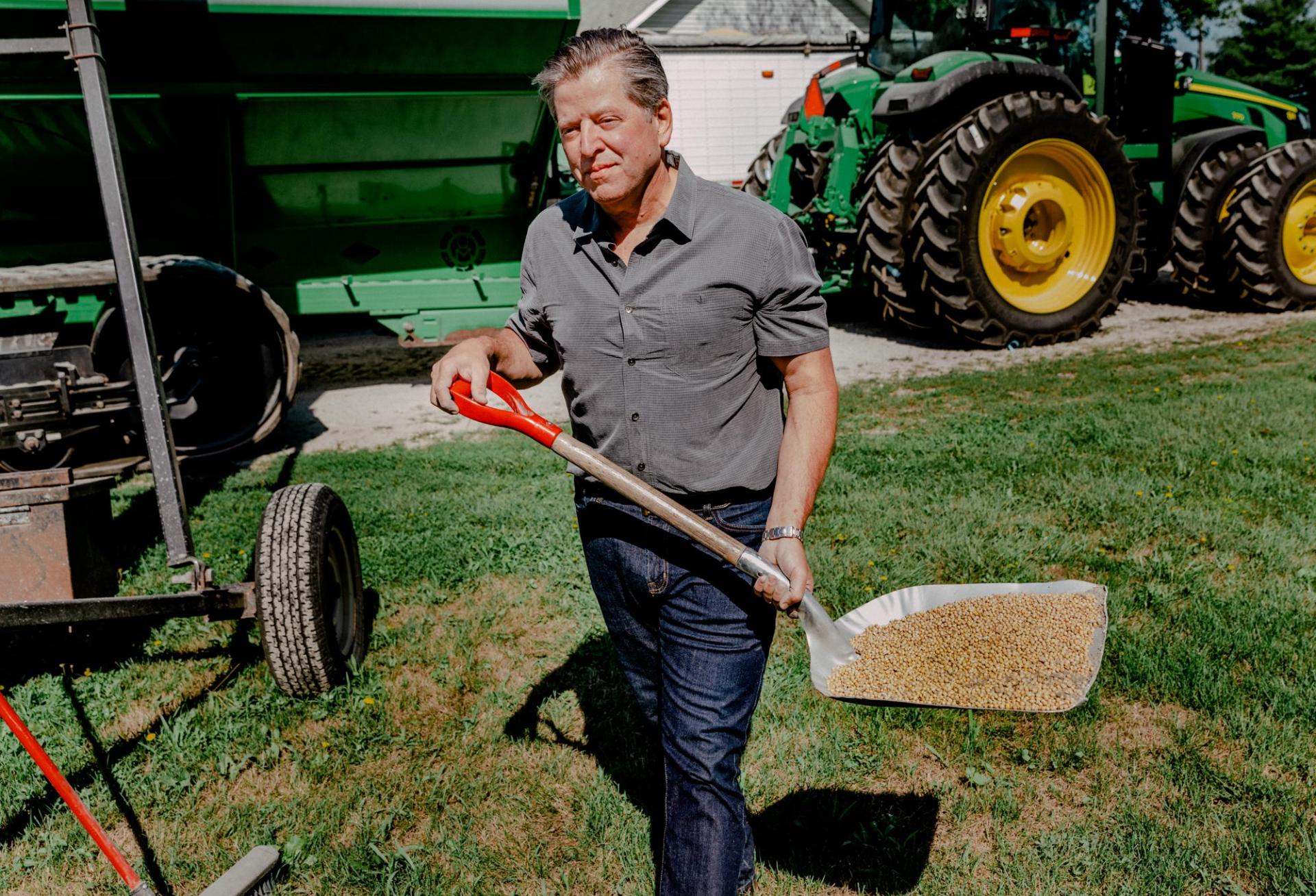 Farmland Partners Founder and Chairman Paul Pittman working on a farm with a shovel, seeds and tractors in the background.
