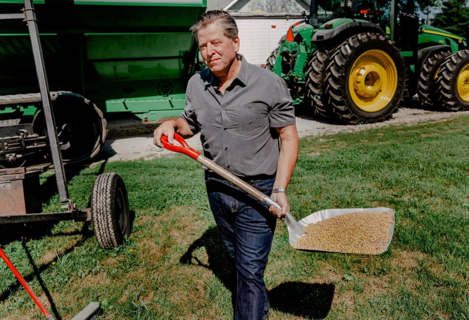 Farmland Partners Founder and Chairman Paul Pittman working on a farm with a shovel, seeds and tractors in the background.