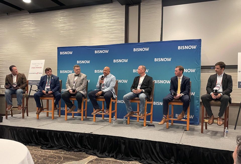 A photograph of panelists seated onstage discussing Colorado aerospace ecosystem