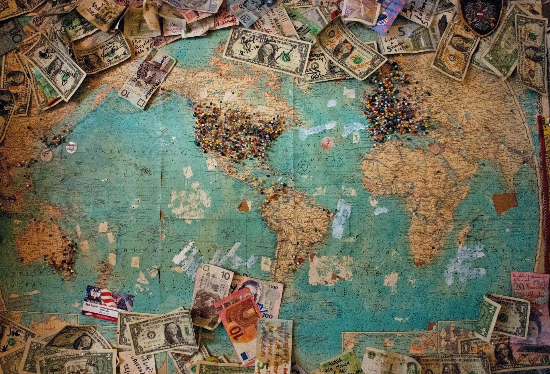 Old world map with pins and currencies left by visitors from all over the planet.