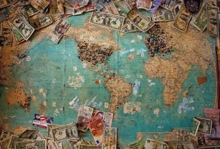 Old world map with pins and currencies left by visitors from all over the planet.