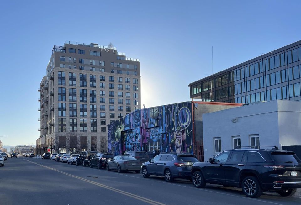 The view of Edit, a large multifamily property, and other RiNo ground-level retail from 3525 Walnut St. with the sun setting behind the multifamily building.