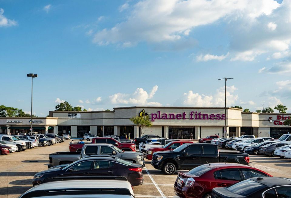 The exterior of a Planet Fitness gym in a strip mall with cars in the parking lot