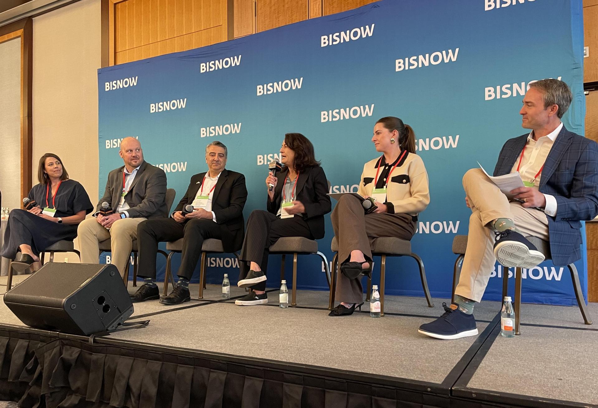 A photograph of panelists speaking at Bisnow's Denver-Boulder Life Sciences Summit, seated in front of a Bisnow-branded step-and-repeat.