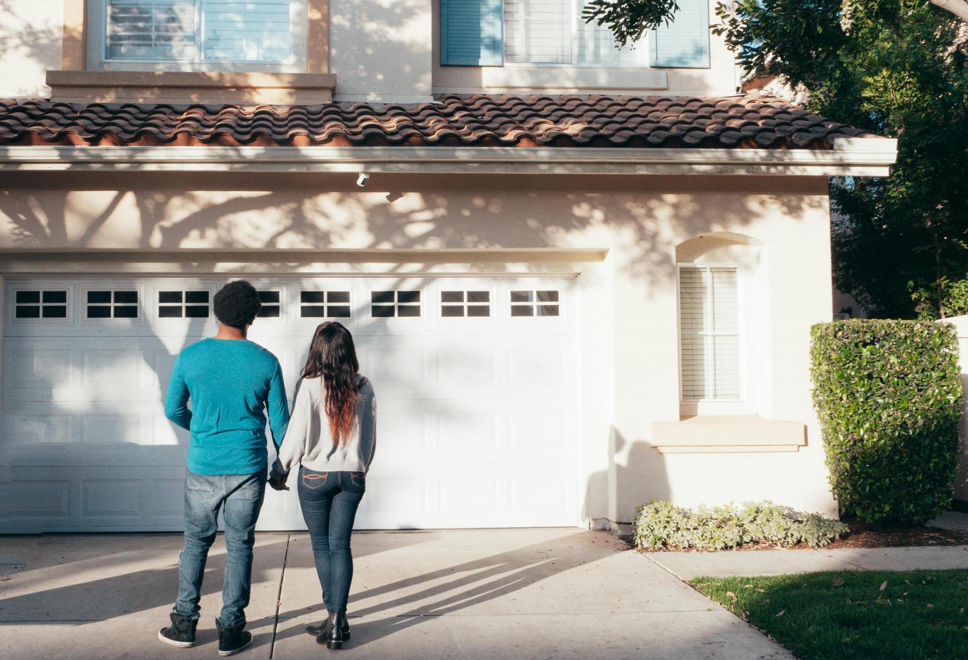 The median age of first-time homebuyers is at an all-time high. A couple standing in the driveway of a two-story southwest-style home.