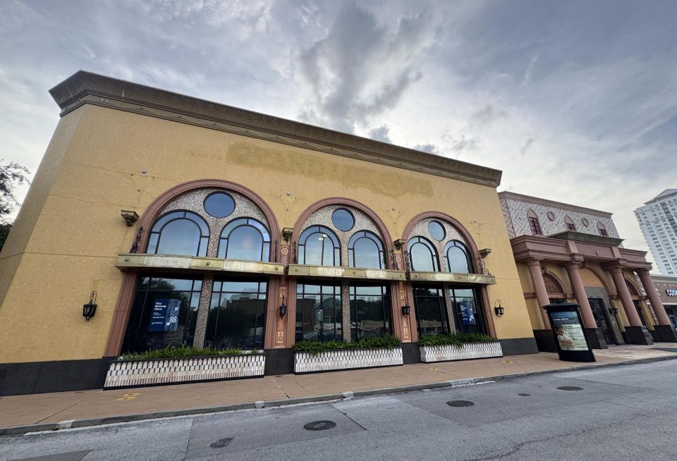 A large vacant storefront with removed signage against an overcast sky 