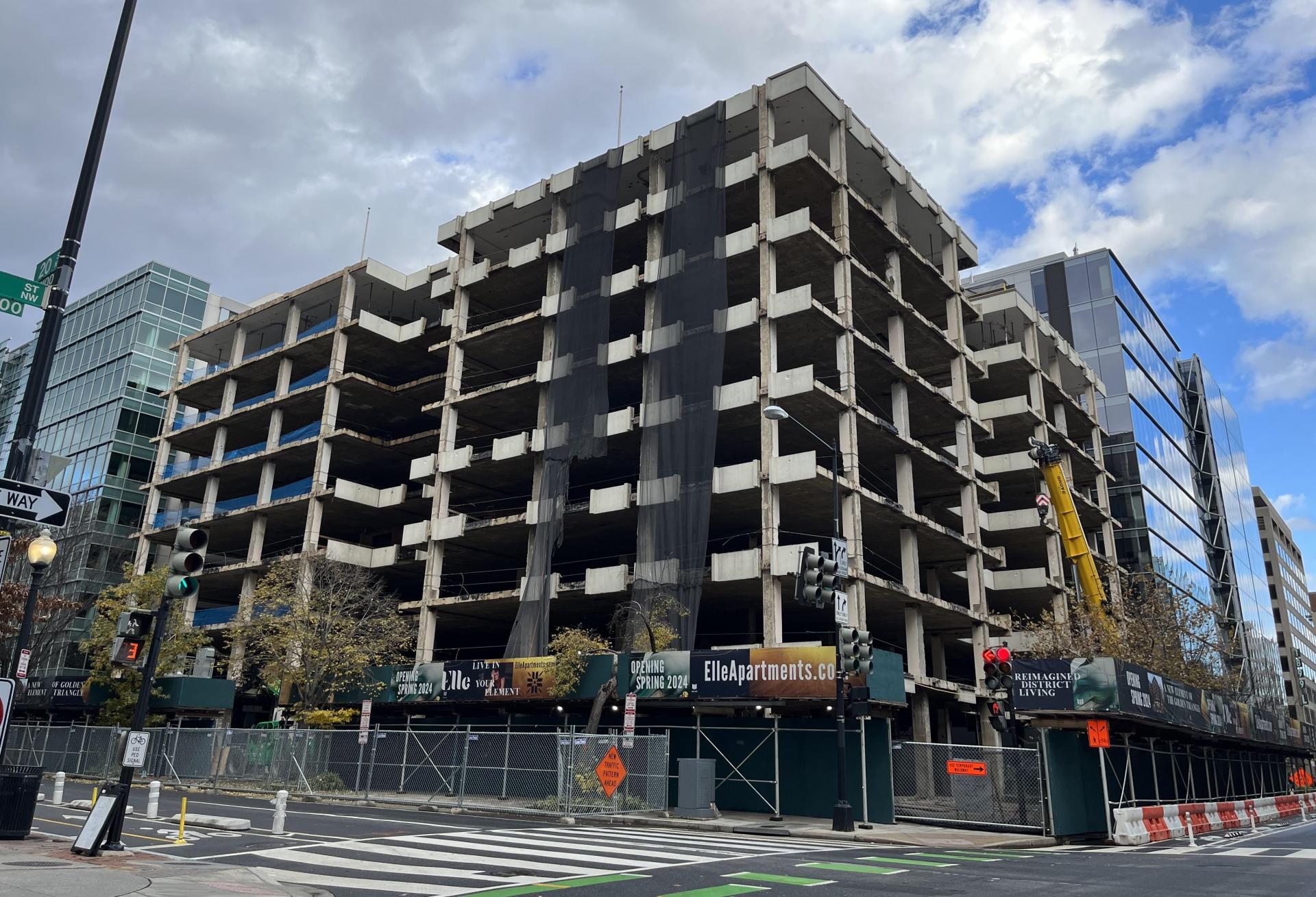 An eight-story building with its outer shell removed and interior visible. Construction is ongoing at the site, which has a sign reading 