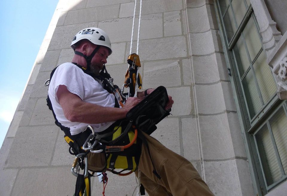 Klein & Hoffman Chief Inspector Mark Danielson hangs from ropes as he inspects a building.