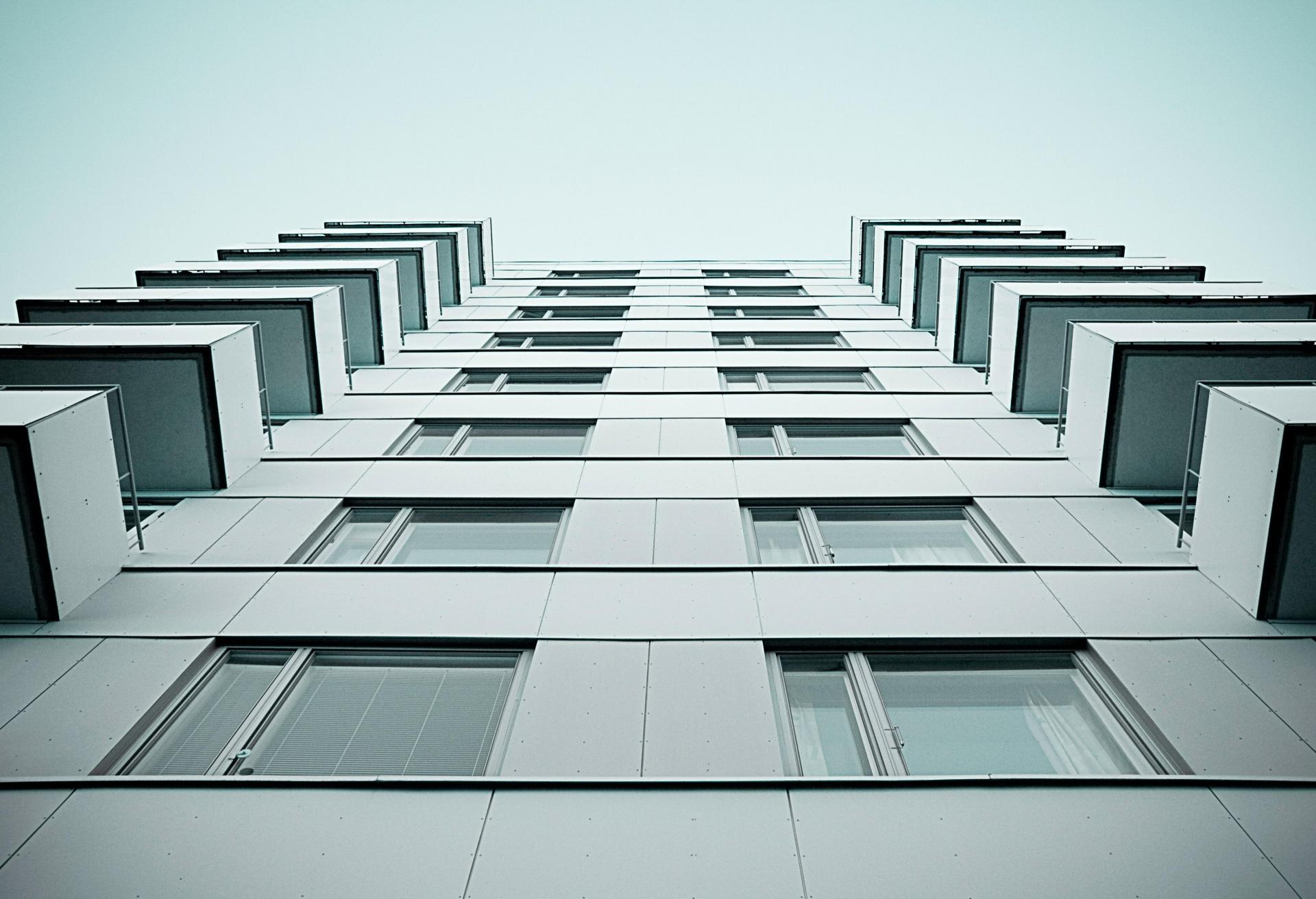Low-angle view of a modern high-rise building with a symmetrical facade, featuring multiple windows and balconies against a clear sky.