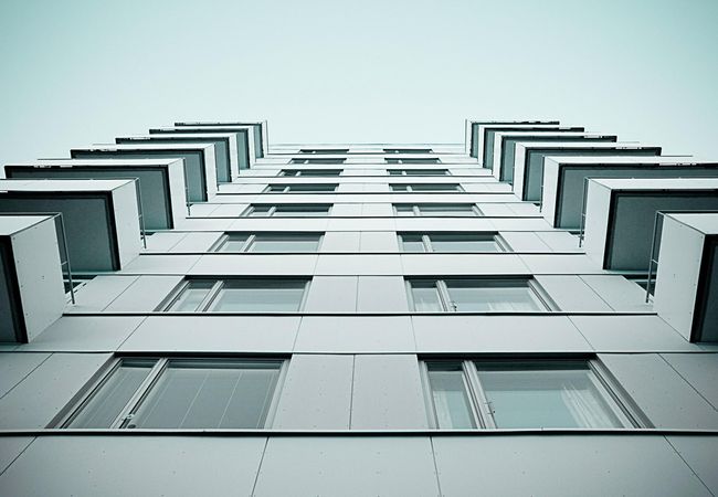 Low-angle view of a modern high-rise building with a symmetrical facade, featuring multiple windows and balconies against a clear sky.