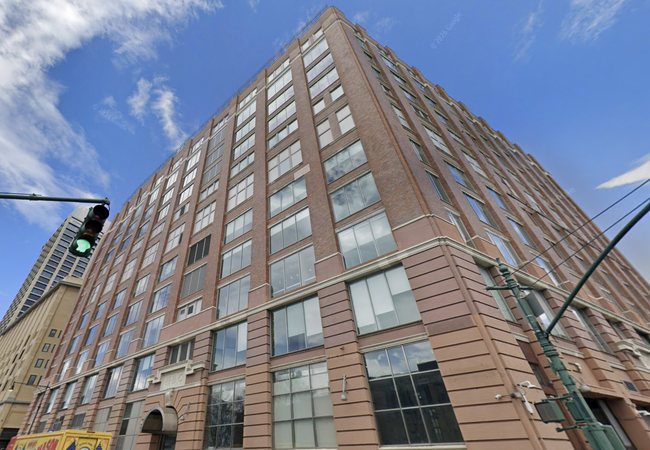A tall brick building with numerous windows against a blue sky, viewed from a low angle. A green traffic light is visible on the left.