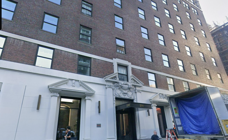 A red brick building with multiple windows, ornate entrance labeled "200," and a truck with a blue tarp unloading at the front.