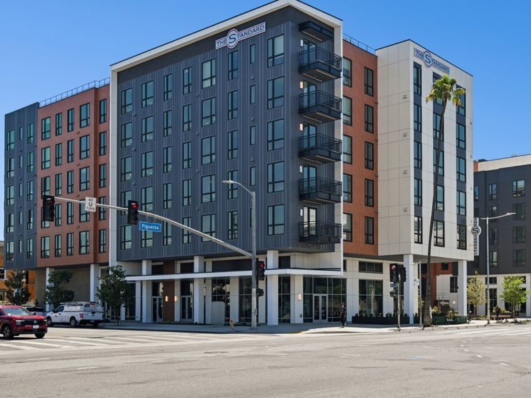 A mid-rise building at a city intersection, featuring large windows and balconies. Also visible are cars and traffic lights under a clear sky.