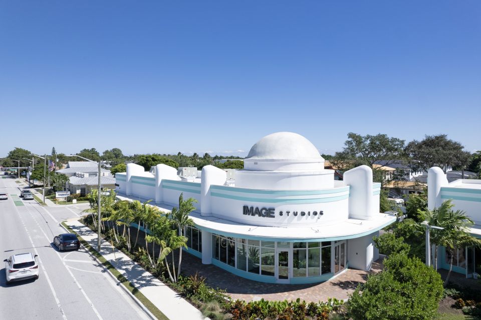 White building with Art Deco design, turquoise accents, and a domed roof labeled "Image Studios," surrounded by palm trees and located on a street corner.