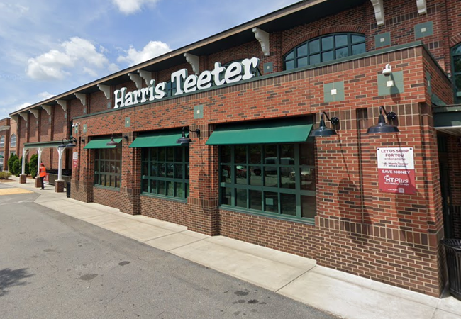 Brick facade of a grocery store with green awnings and a sign above. Sidewalk and parking lot visible under a partly cloudy sky.