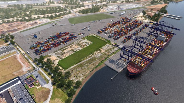 Aerial view of a busy container port with large cranes, numerous colorful shipping containers, trucks, a docked cargo ship, and adjacent green areas.