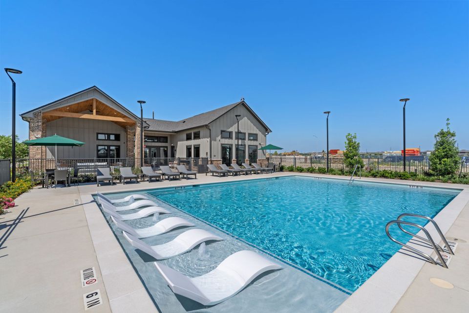 Outdoor swimming pool with chaise lounge chairs and umbrellas beside a modern clubhouse on a sunny day.