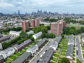 Aerial view of an urban neighborhood with rows of houses and tall apartment buildings, set against a city skyline under a cloudy sky.