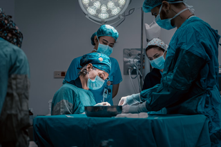 Surgical team in an operating room, focused and wearing scrubs, masks, and caps, under bright operating lights.