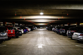 A dimly lit, spacious indoor parking garage with cars parked neatly on both sides and a single directional arrow on the concrete floor.