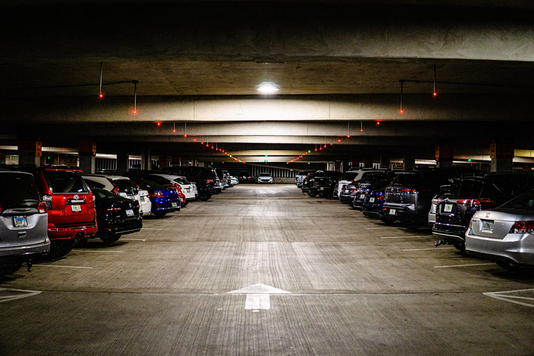 A dimly lit, spacious indoor parking garage with cars parked neatly on both sides and a single directional arrow on the concrete floor.