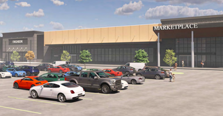 A busy mall parking lot with various cars parked in front of a large shopping complex labeled "Marketplace" under a partly cloudy sky.