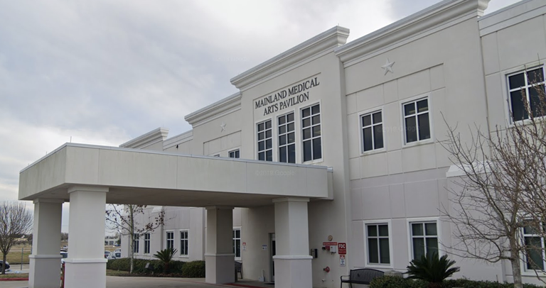 A beige, two-story building with a covered entrance labeled "Mainland Medical Arts Pavilion" against a cloudy sky, surrounded by trees and plants.