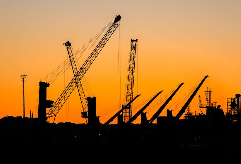Silhouettes of cranes at a construction site against an orange sunset sky.