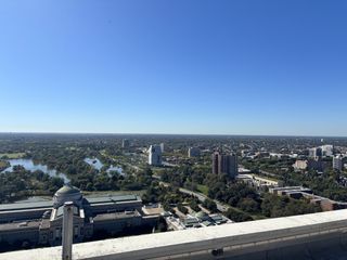 A panoramic view of a city with green spaces, lakes, and buildings, under a clear blue sky.
