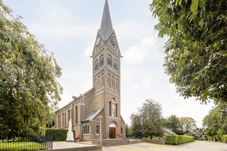 A brick church with a tall clock tower and spire, surrounded by trees; a statue is in the foreground.