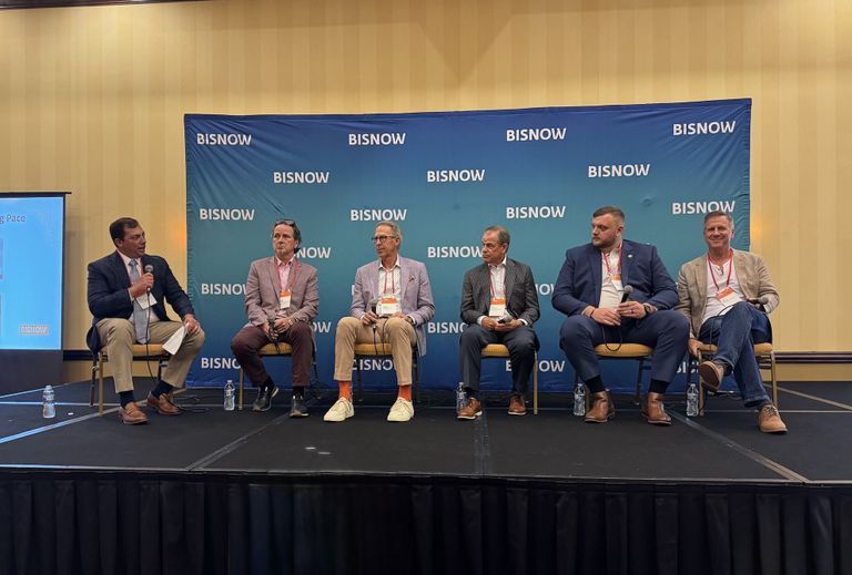 Six men sit on stage during a panel discussion at a Bisnow event, with a backdrop displaying the Bisnow logo.