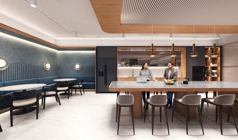 Modern office kitchen with a large island, bar stools, and a cozy seating area. Two people are having a conversation near a laptop.
