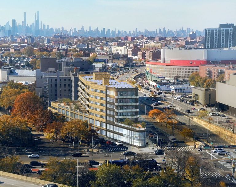 Aerial view of a busy urban area with modern buildings, autumn trees, and distant city skyline under a clear blue sky.