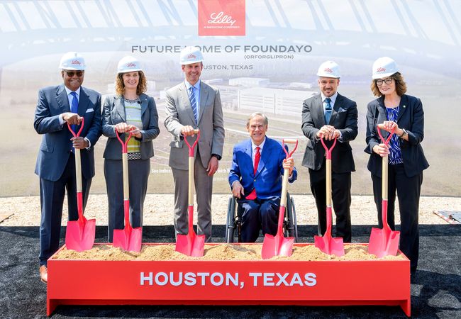 Six people in hard hats participating in a groundbreaking ceremony with shovels, standing in front of a sign reading "Future Home of Foundayo, Houston, Texas."