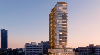 Tall modern skyscraper with glass facade in an urban setting, captured during sunset, with buildings and a road in the foreground.