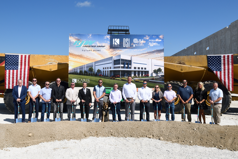 A group of people standing with shovels at a groundbreaking ceremony in front of a construction sign, flanked by American flags.