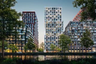 Modern high-rise buildings with numerous windows and balconies, surrounded by trees, are reflected in a calm water body at twilight.