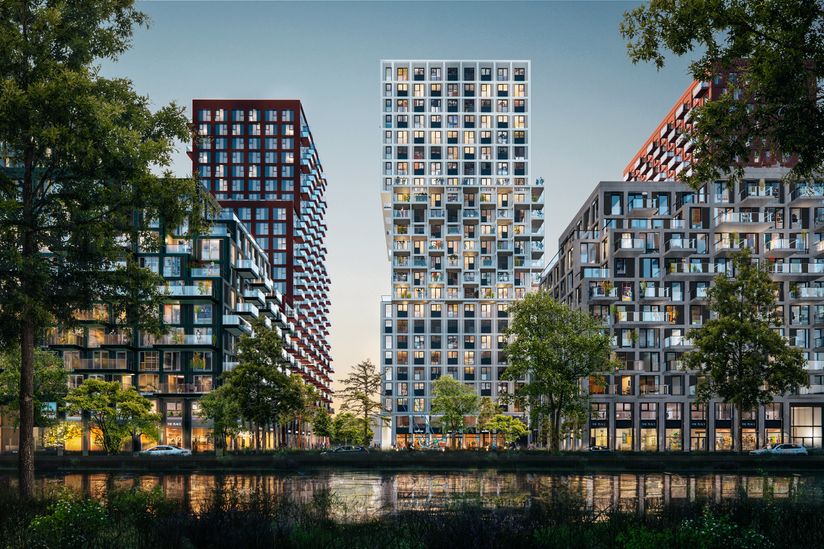Modern high-rise buildings with numerous windows and balconies, surrounded by trees, are reflected in a calm water body at twilight.
