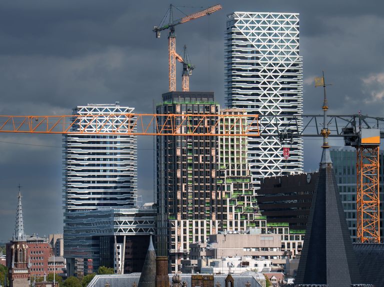 Skyline view with modern skyscrapers under construction, featuring cranes and geometric facade designs, against a cloudy sky.