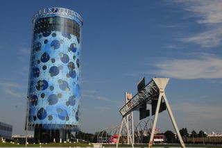 A modern cylindrical building with a blue circular pattern, adjacent to highway signage and a Burger King logo under a clear sky.