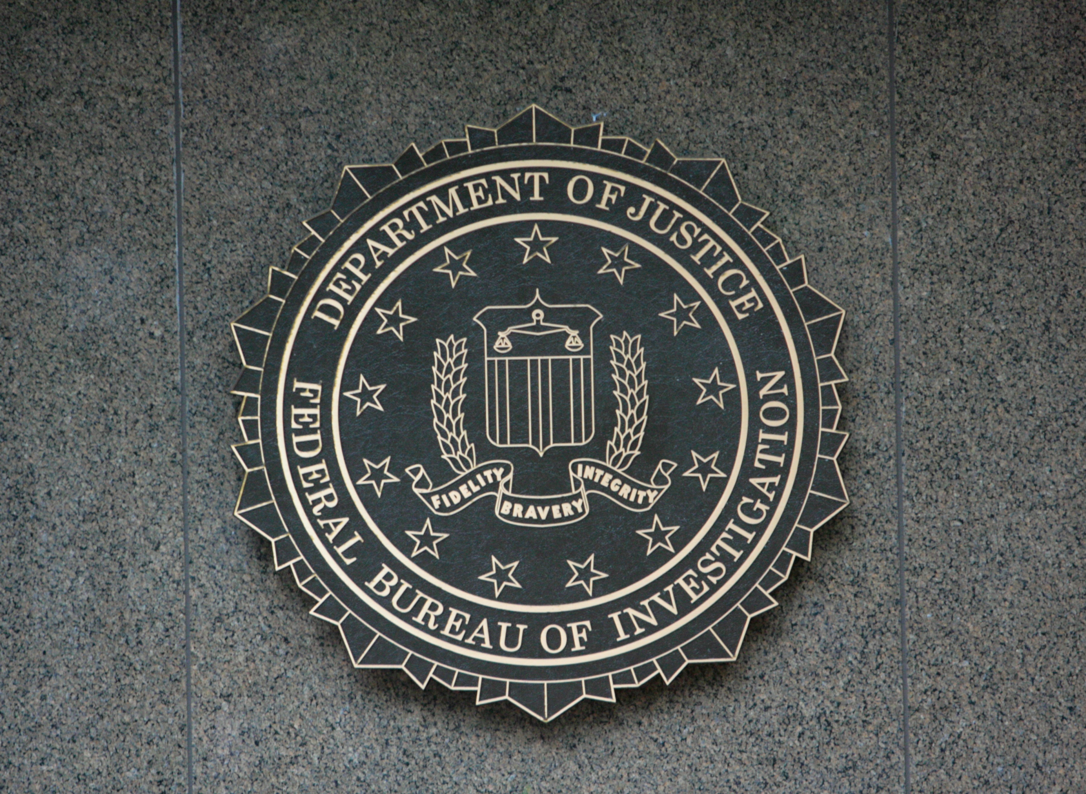 The FBI seal displayed on a gray stone wall, featuring stars, a shield, and an eagle with the words "Fidelity, Bravery, Integrity."