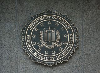 The FBI seal displayed on a gray stone wall, featuring stars, a shield, and an eagle with the words "Fidelity, Bravery, Integrity."