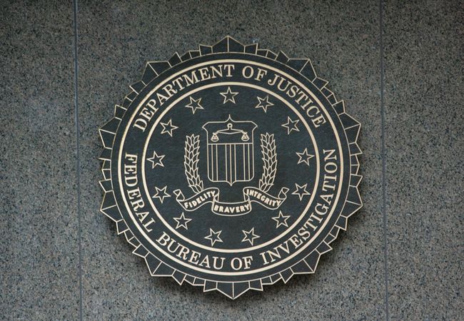 The FBI seal displayed on a gray stone wall, featuring stars, a shield, and an eagle with the words "Fidelity, Bravery, Integrity."