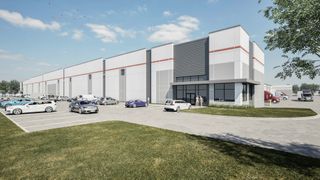 Modern industrial warehouse with a large parking lot, cars, and trucks under a clear blue sky. People are standing near the entrance.