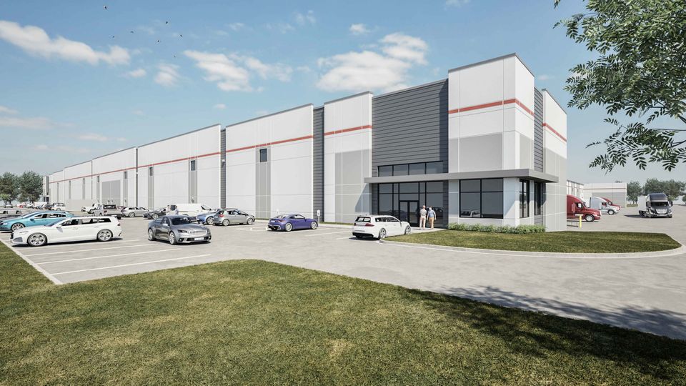 Modern industrial warehouse with a large parking lot, cars, and trucks under a clear blue sky. People are standing near the entrance.